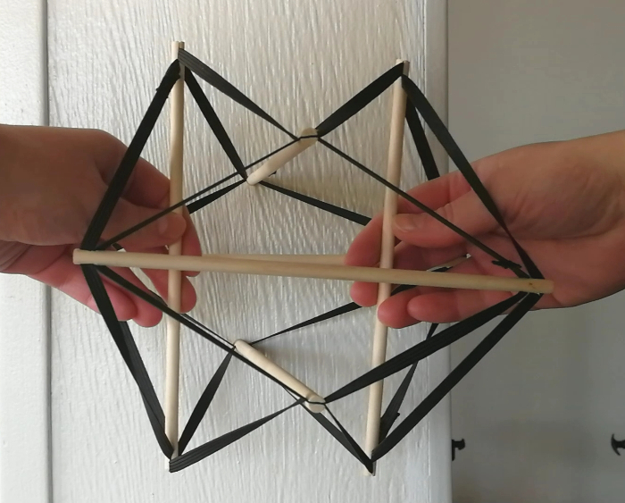 Tensigritetsmodel_neutral Tensigritetsmodel i neutral position. I modellen svarer pindene til knoglerne, og elastikkerne svarer til de myofasciale kæder. Modellen kan ses som en model for vores krop. Den viser, hvordan kroppen kan opretholde sin balance ved at fordele spændingen i helheden. På den måde kan kroppen holde sig oprejst og kollapser ikke under tyngdekraften.